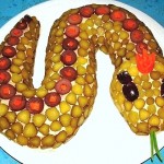 Салат выложен как змея из оливок и долек отварной свеклы. Из морковки вырезана корона, а язык из двух перьев лука